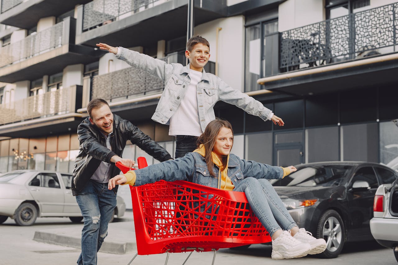 Cheerful family enjoying a fun day outside with a shopping cart ride in an urban setting.