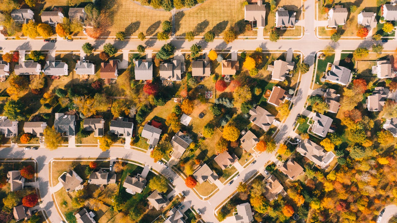 Drone view of dwelling houses between colorful meadows with trees and wavy roads in suburb