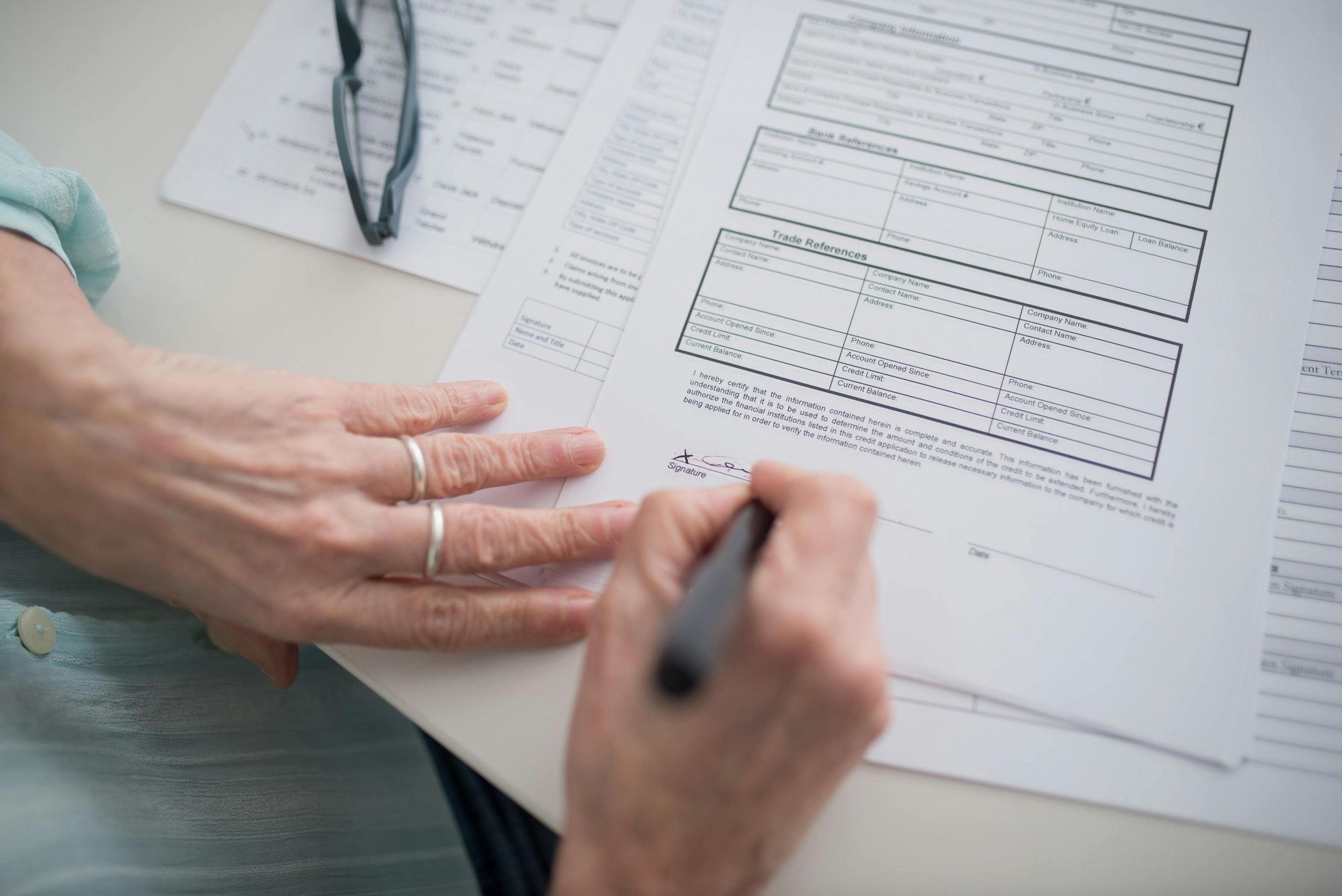 A close-up view of a hand signing official documents with a pen indoors.