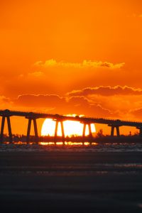 Dramatic sunset casting a vivid orange glow behind a Florida bridge silhouette.