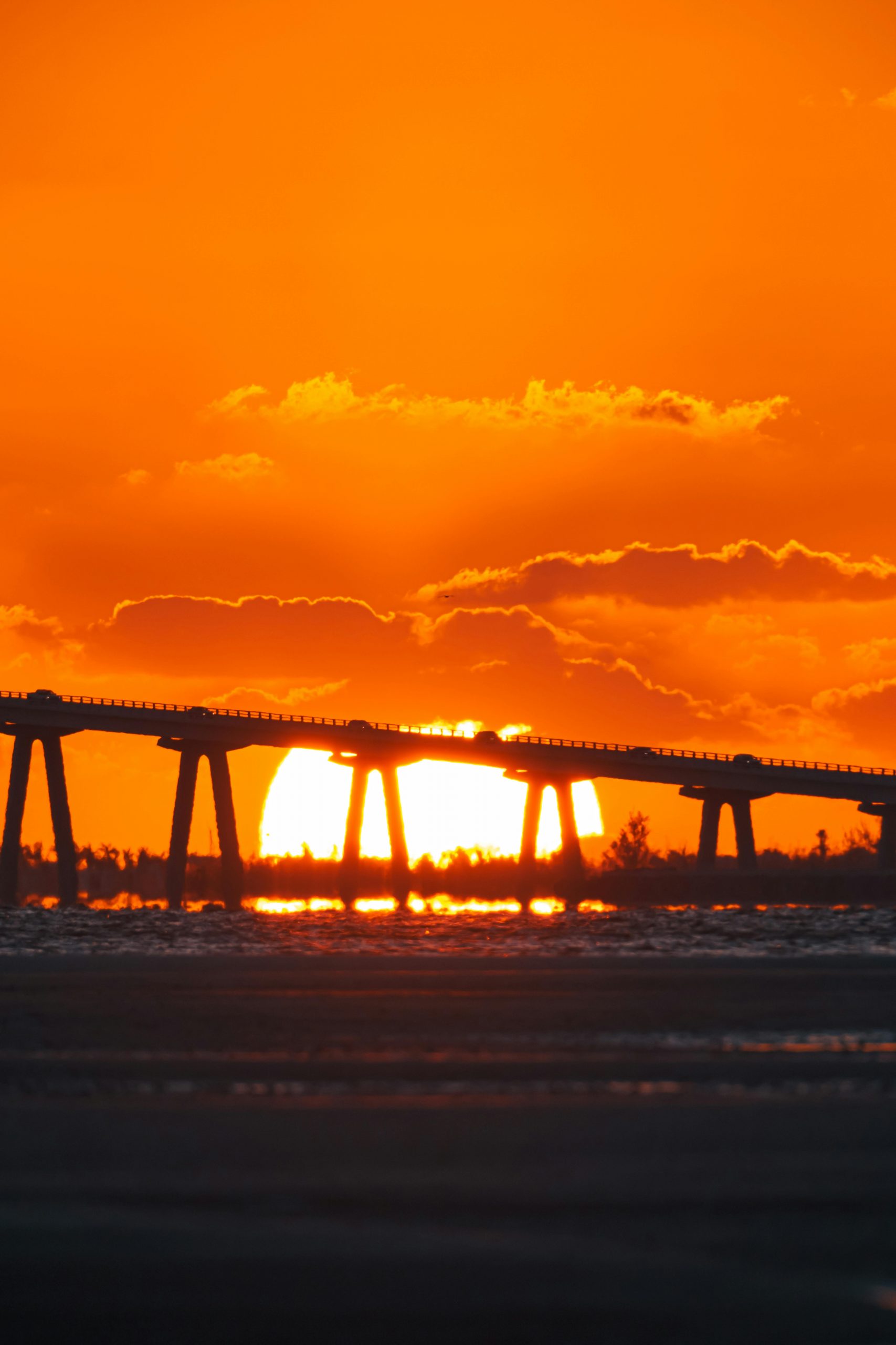 Dramatic sunset casting a vivid orange glow behind a Florida bridge silhouette.